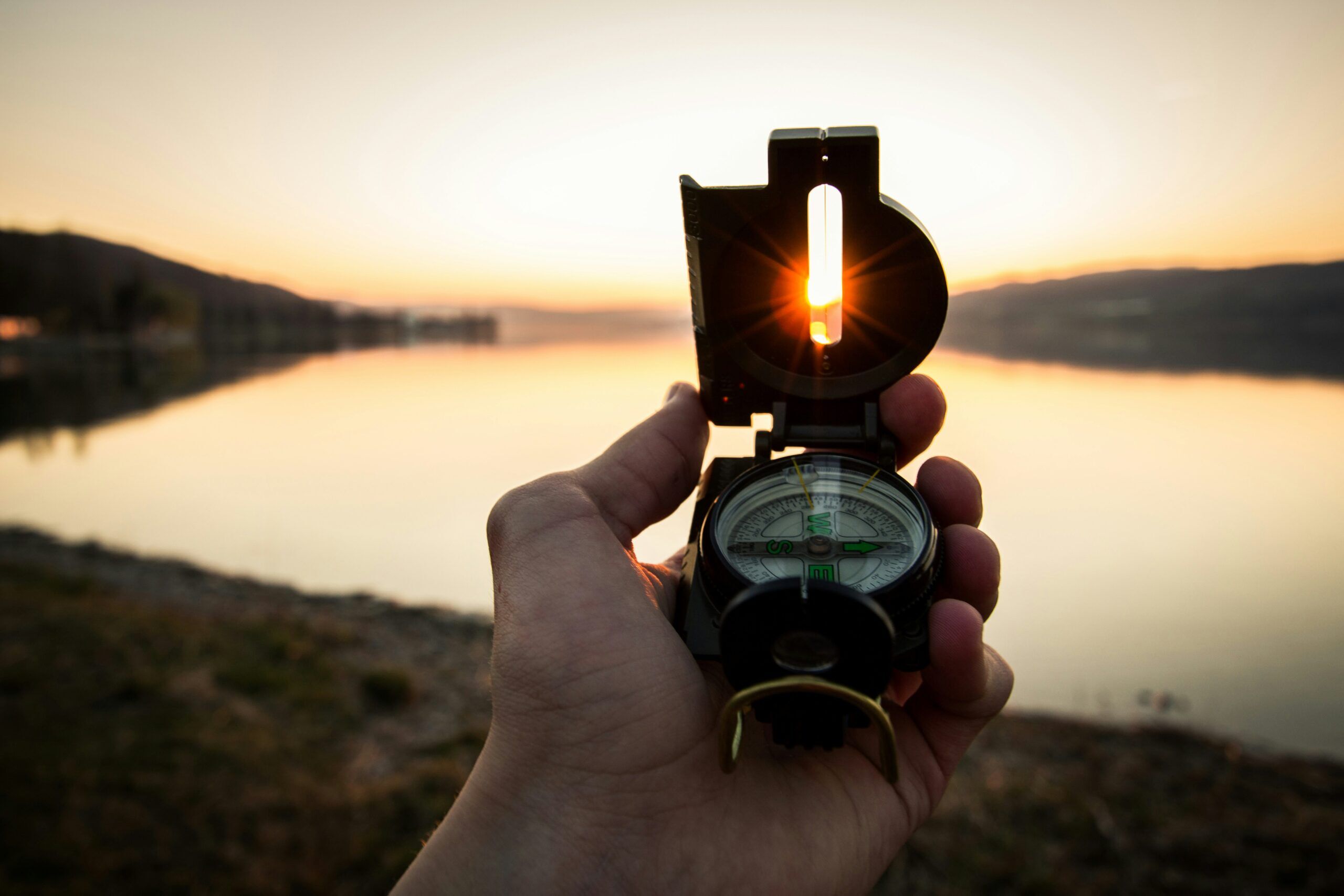 A handheld compass aligned with the setting sun over a calm lake, used as a metaphor for SQL Server wait statistics as directional signals that require context before making performance decisions.